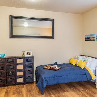 A cozy bedroom with a bed adorned in blue and yellow accents, featuring a large mirror above a wooden dresser.