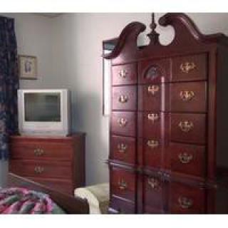 A bedroom with a wooden armoire and a dresser topped with a television.