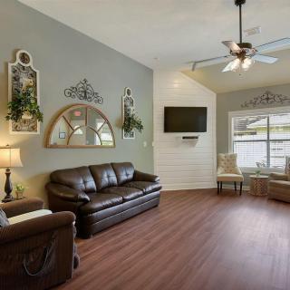 A cozy living room with elegant furniture and decor, featuring a leather sofa, armchairs, a television mounted on the wall, and a ceiling fan.