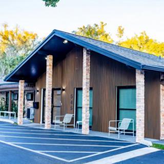 A small building with a sloped roof, surrounded by trees and a parking lot.