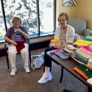 Two elderly women sitting indoors, enjoying a knitting session with colorful yarn.