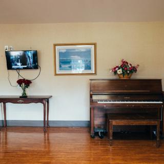 A cozy living room with a piano, wall-mounted television, and decorative flowers on a table.