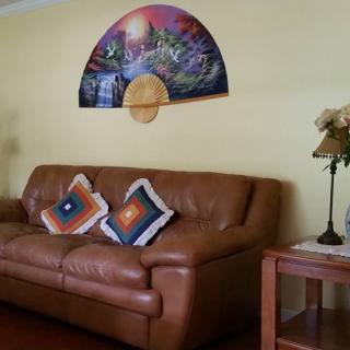 A cozy living room with a brown leather sofa, colorful decorative pillows, a stylish wall art piece, and a small lamp on a side table.