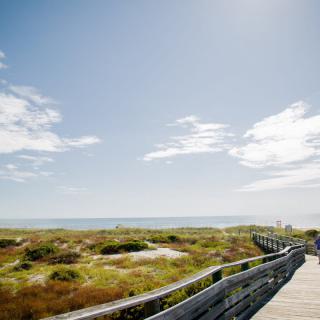 A scenic boardwalk leading to a beautiful beach under a clear blue sky.