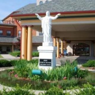 A white statue stands in the middle of a garden in front of a building.