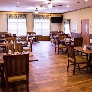 An empty restaurant dining area with neatly arranged tables and wooden flooring.