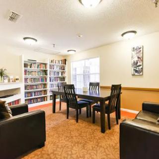 A cozy reading area featuring a bookshelf filled with books, a wooden table surrounded by chairs, and comfortable seating.