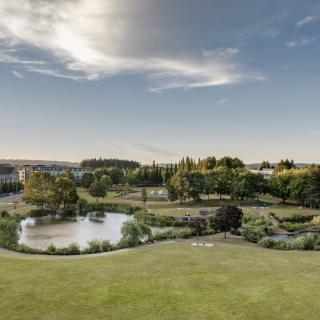 A serene landscape featuring a pond surrounded by trees and grass under a partly cloudy sky.