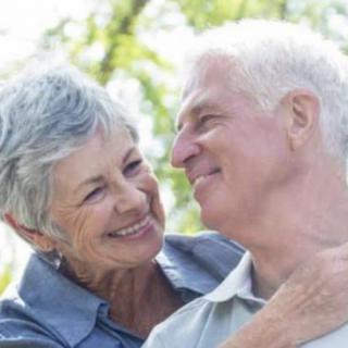 A joyful elderly couple smiling at each other outdoors.