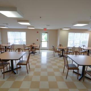 An empty dining hall with tables and chairs arranged neatly on a checkered floor.