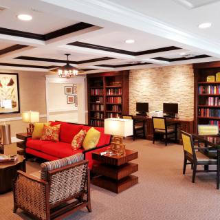 A cozy library living room with a red sofa, bookshelves, and computer stations.