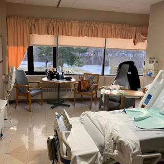 A view of a hospital patient room featuring a bed, chairs, and medical equipment.