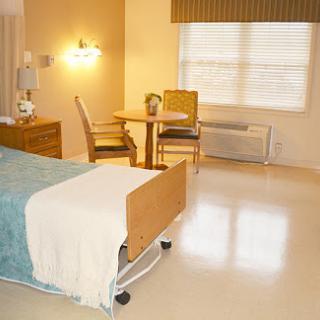 A bright and clean hospital room with a bed, table, and chairs.