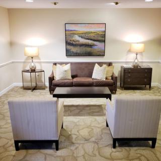 A cozy living room setup with a sofa, two chairs, and a coffee table, complemented by art on the wall and warm lighting from lamps.