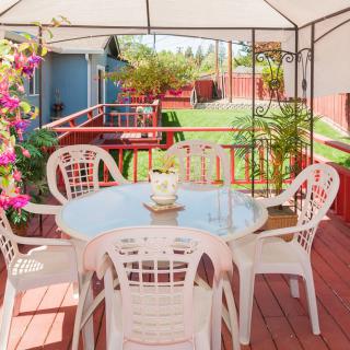 A cozy outdoor patio with a table and chairs under a pergola, surrounded by a lush garden.