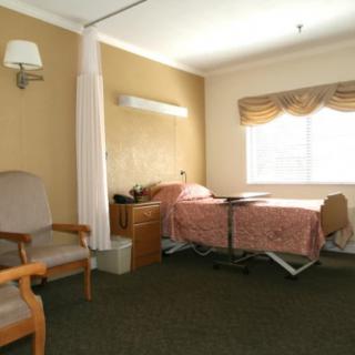 A hospital room with a bed, chair, and window with curtains.
