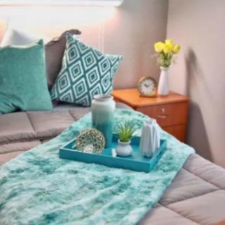 A cozy bedroom setup with teal accents, featuring decorative pillows and a tray with candles on the bed.