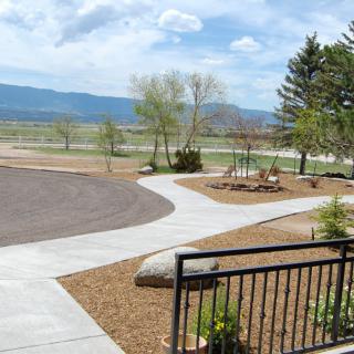 A scenic outdoor landscape with a pathway, trees, and distant mountains under a partly cloudy sky.