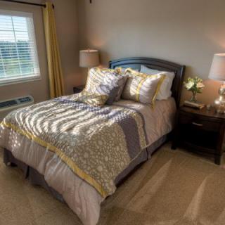 A cozy bedroom with a neatly made bed, soft lighting from table lamps, and a window letting in natural light.