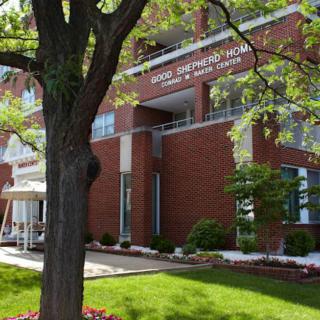 A hospital building with a prominent tree and well-maintained landscaping in the foreground.