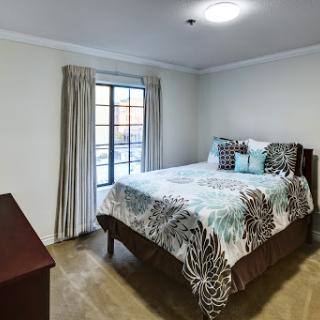 A cozy bedroom featuring a queen-sized bed with decorative pillows and light curtains.