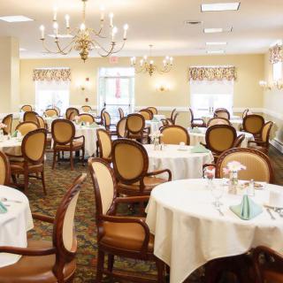 An elegant dining room with neatly arranged tables and chairs, featuring chandeliers and soft lighting.