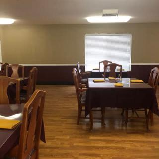 An empty dining room with tables and chairs neatly arranged, featuring wooden floors and napkins placed on the tables.