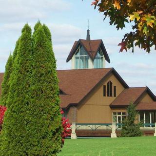 A picturesque building surrounded by lush greenery and trees under a partly cloudy sky.