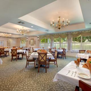 An elegant dining room with chandeliers and set tables, offering a scenic window view.