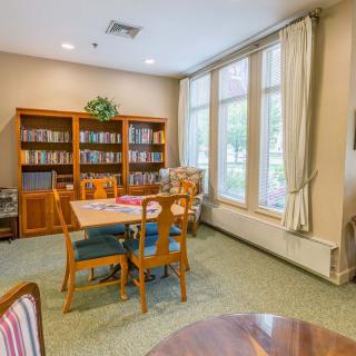 A cozy reading room with bookshelves, a table, and chairs by large windows.