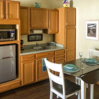 A compact kitchen with wooden cabinets, stainless steel appliances, and a dining table set for two.