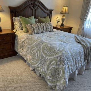 A cozy bedroom with a neatly made bed, featuring patterned bedding and several decorative pillows, flanked by wooden nightstands topped with lamps.