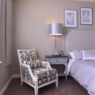 A cozy and elegantly designed bedroom featuring a patterned chair, stylish lamp, and a neatly made bed.