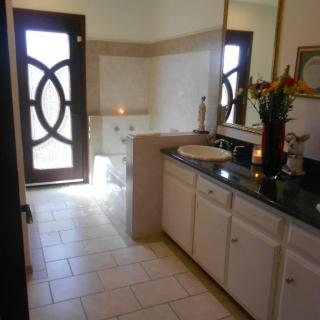 A well-lit bathroom featuring a sink with a large mirror, a stylish door, and a bathtub.