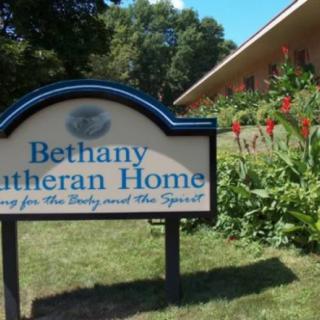 A sign for Bethany Lutheran Home with a garden and building in the background.