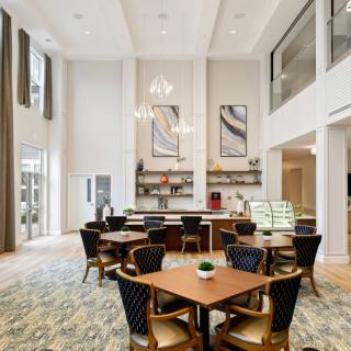 A modern dining space with high ceilings, featuring elegant tables and chairs, large windows, and decorative artwork.