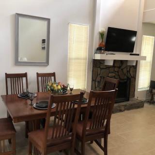 A cozy dining area with wooden furniture, featuring a table and chairs next to a fireplace and TV.