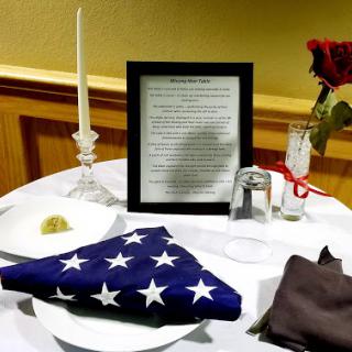 A formal dining table set up for a memorial event, featuring an American flag, roses, and a candle.