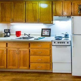 A cozy kitchen with wooden cabinets, a stove, refrigerator, and countertop space.