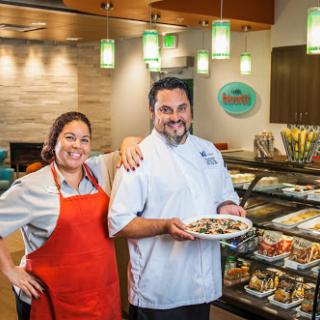 Two chefs proudly present a dish in a vibrant restaurant setting.