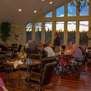 A cozy dining room with seniors enjoying a meal and conversation as the sun sets outside.