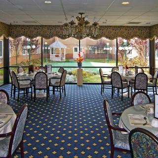 A neatly arranged dining room with elegant tables and chairs, offering a scenic view of a garden through large windows.