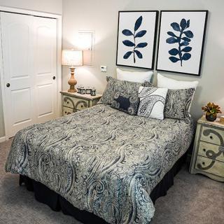 A neatly arranged bedroom featuring a patterned bedspread, two nightstands with lamps, and framed leaf artwork above the bed.