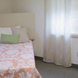 A cozy bedroom with a neatly made bed, pillows, and light-filtering curtains.