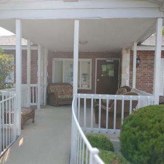 A covered porch with a ramp, featuring outdoor seating and a brick wall.