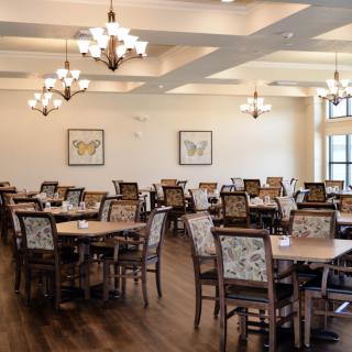 A well-lit dining area with several tables and chairs arranged neatly, featuring elegant chandeliers and wood flooring.