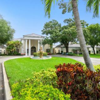 A picturesque building with a circular driveway surrounded by lush greenery and palm trees.