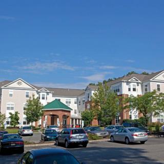 A residential apartment complex with a parking lot filled with cars on a sunny day.