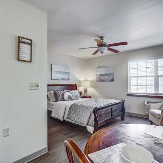 A cozy bedroom with a bed, table, ceiling fan, and artwork on the walls.