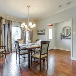 A cozy dining room with a wooden table and chairs, illuminated by a chandelier, featuring hardwood floors and elegant curtains.